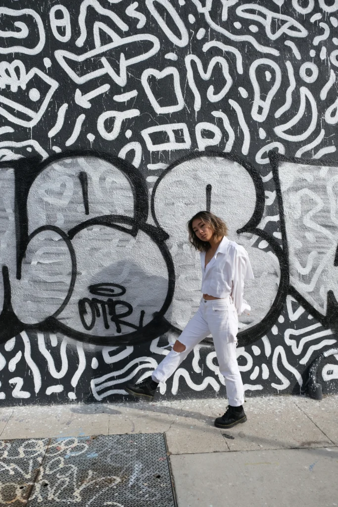 A Japanese girl wearing Japanese street style clothing posing on the street with a graffiti wall